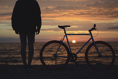 silhouette person beside hardtail bike on gray sand during sunset thumbnail