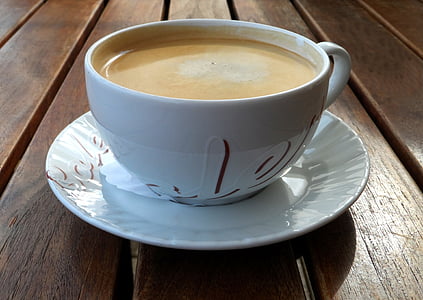 white ceramic cup filled with latte on round white ceramic saucer on brown wooden surface thumbnail