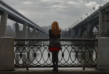 woman wearing black jacket standing beside black metal rails watching concrete bridge thumbnail