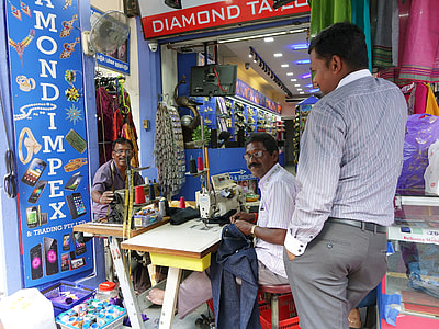 man standing near another man sewing clothes thumbnail
