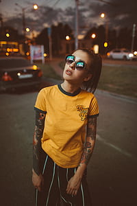 selective focus photography of woman looking up on billboard wearing yellow crew-neck shirt and hippie sunglasses standing on road thumbnail