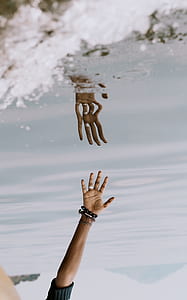 person reaching body of water with his hand reflection photography thumbnail