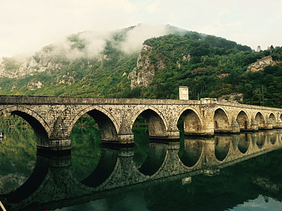 gray concrete bridge over body of water near mountain under white sky at daytime thumbnail