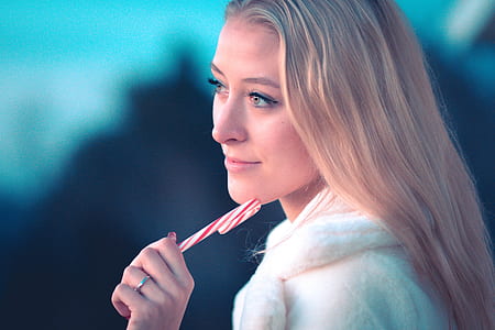 selective focus photography of woman wearing white coat holding candy cane thumbnail