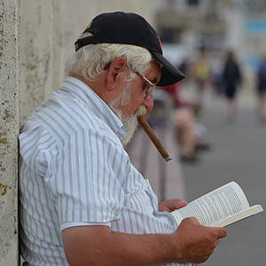man in white shirt with tobacco and black hat while reading book thumbnail