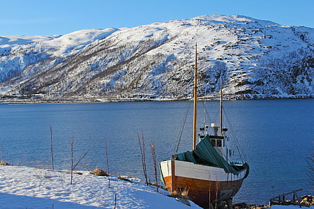 brown and white boat near the snowy mountain thumbnail