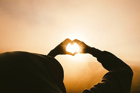 silhouette photo of person forming heart shape at the sun thumbnail