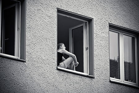 grayscale photo of woman standing beside window thumbnail