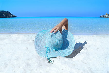 person holding blue wicker sun hat while laying on white sand during daytime thumbnail