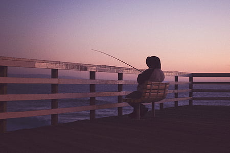 photo of person sitting on bench and holding fishing rod thumbnail