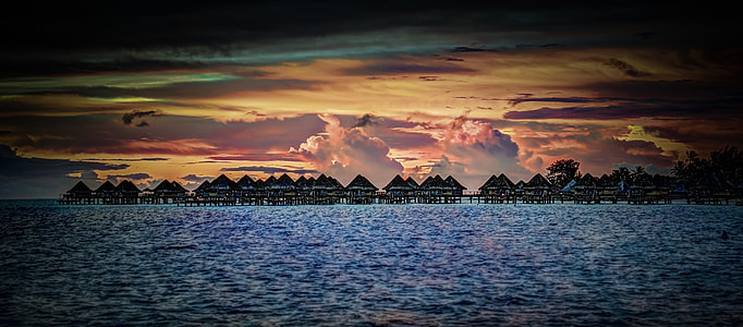 silhouette of nipa huts on body of water thumbnail