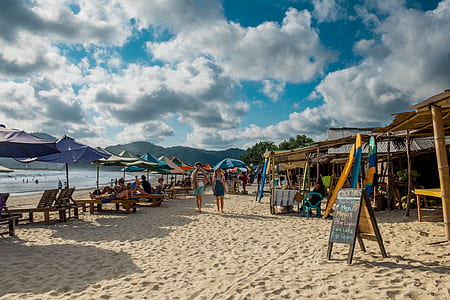 two person walking across beach stalls near beach under white cloudy skies thumbnail