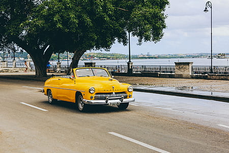 classic yellow convertible coupe travelling on road during daytime thumbnail