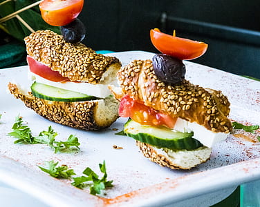 bun with sesame seeds and sliced cucumber, tomatoes, and raisins on plate thumbnail