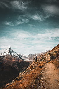 man carrying black backpack standing on cliff of mountain thumbnail