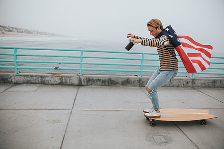man in brown sweater holding america flag on brown longboard during daytime thumbnail