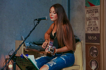 woman playing on guitar while sitting on chair with microphone next to her thumbnail