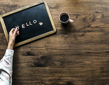 flat lay photography of person's hand on hello board beside mug thumbnail