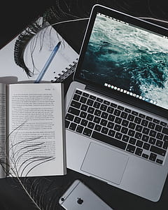turned on silver MacBook beside open book thumbnail