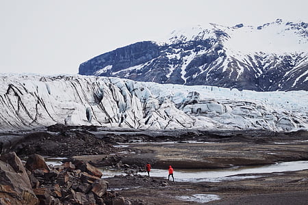two people walking on brown sand near mountain covered with snow thumbnail