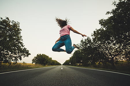 woman jumping on highway near trees thumbnail