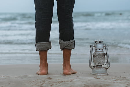 Person Standing on Shoreline Beside Gray Tubular Lantern thumbnail