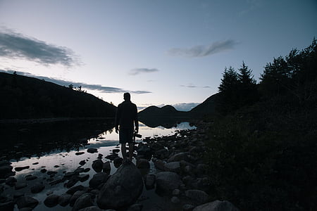 man standing on calm lake under grey sky thumbnail