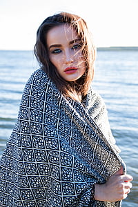 woman covering white and black towel stands near body of water at daytime thumbnail