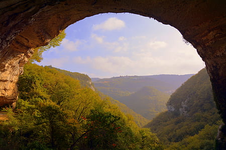 cave near green mountains under cloudy sky thumbnail