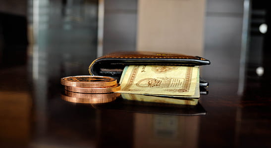 banknote inside brown leather bifold wallet with gold-colored coins on brown wooden surface in selective focus photography thumbnail