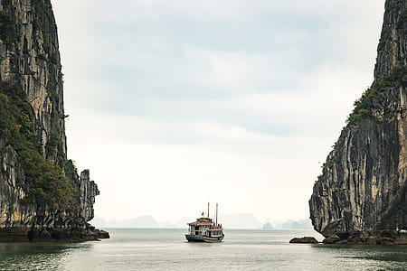 brown and red boat sailing in the middle of two rock cliffs thumbnail