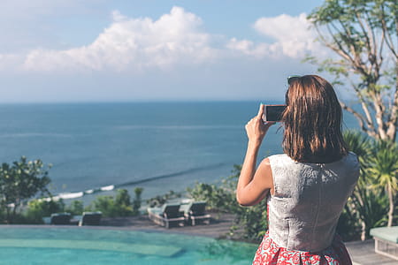 Woman Wearing White and Red Sleeveless Dress Taking Photo of Beach thumbnail