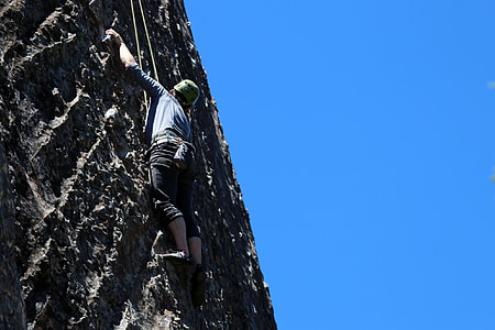 person climbing a cliff while holding a rope during daytime thumbnail