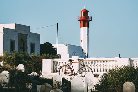 red city bike parked beside white and red concrete lighthouse thumbnail