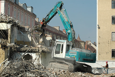 blue and white excavator taking down white concrete house thumbnail