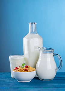 milk in clear glass pitcher, bottle and drinking glass and cereals on white ceramic bowl thumbnail