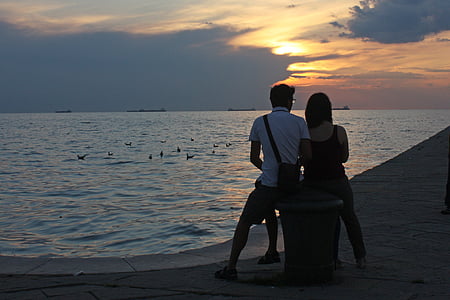 silhouette photography of man and woman sitting on bench near body of water thumbnail
