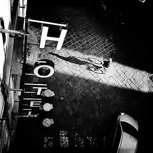 gray scale photo of man riding bicycle beside Hotel building thumbnail