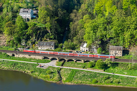 red train traveling on railway near trees thumbnail