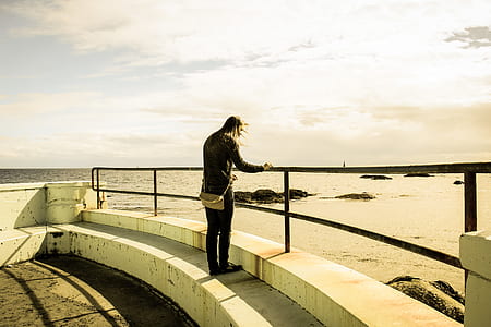 person standing while holding metal fence while facing body of water thumbnail
