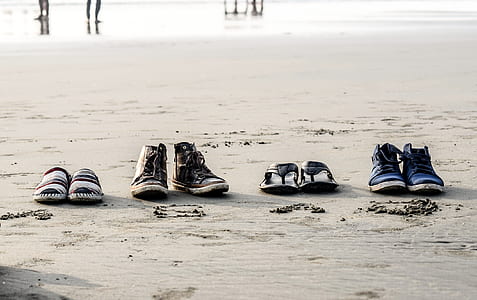 two pairs of shoes and two pairs of sandals on beach sands thumbnail