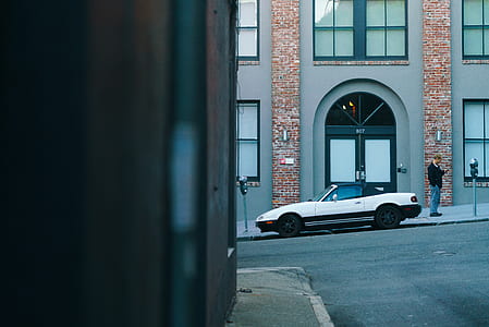 white convertible parked near man standing on front of building thumbnail