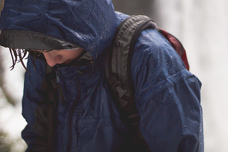 person wearing blue raincoat with backpack looking downward thumbnail