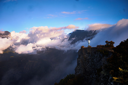 man standing on cliff facing white clouds during daytime thumbnail