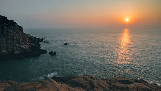 landscape photography of rock formation surrounded by body of water during sunset thumbnail