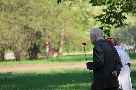 man holding red petaled flower beside woman while walking during daytime thumbnail