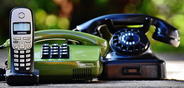 Black and Green Rotary Telephones Beside Cordless Home Telephone thumbnail