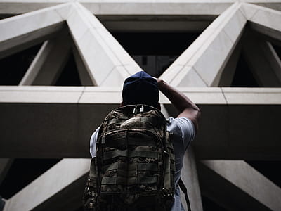 man in white shirt with backpack and blue hat looking up in concrete building during daytime thumbnail