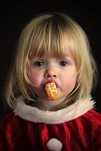 girl biting orange fruit wearing Santa costume thumbnail