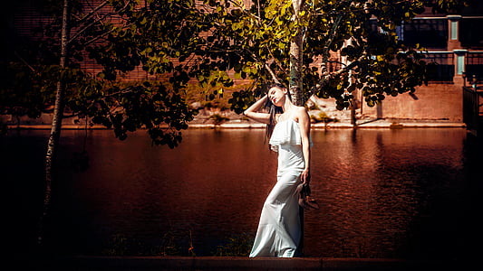 standing woman leaning against tree beside river thumbnail